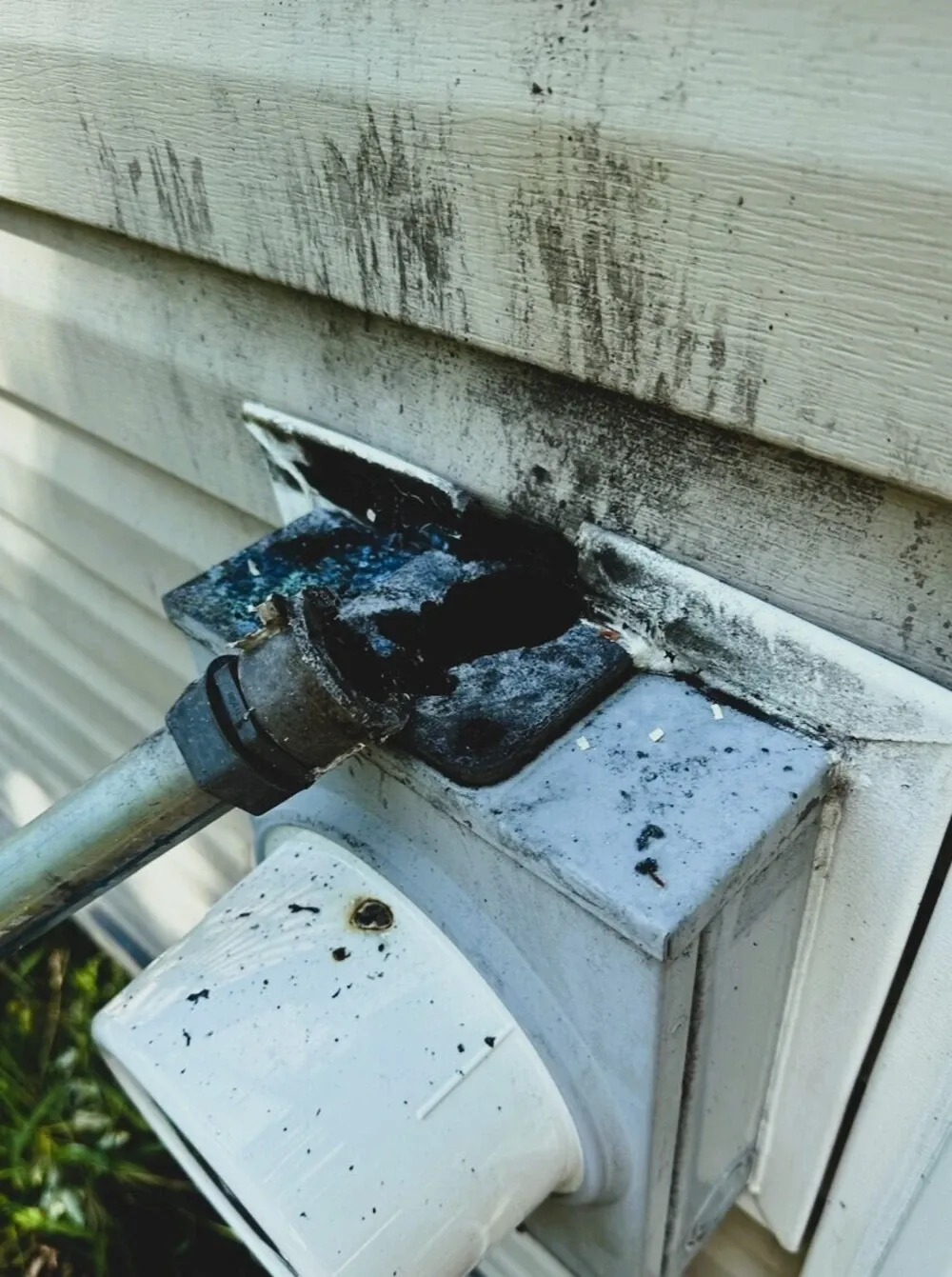 Scorched, damaged electric meter and service mast on a home's siding