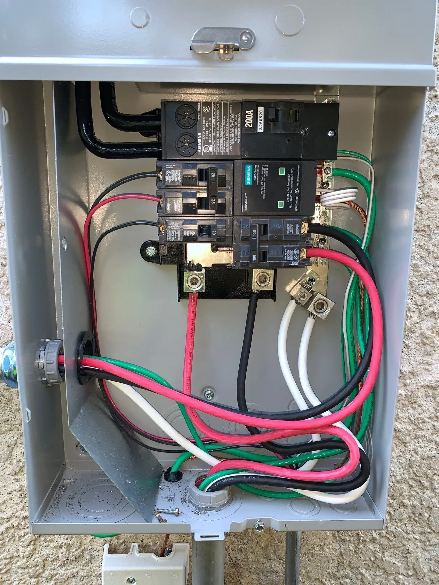 Outdoor electrical box opened to show its breaker and new wiring, mounted on a home's exterior wall