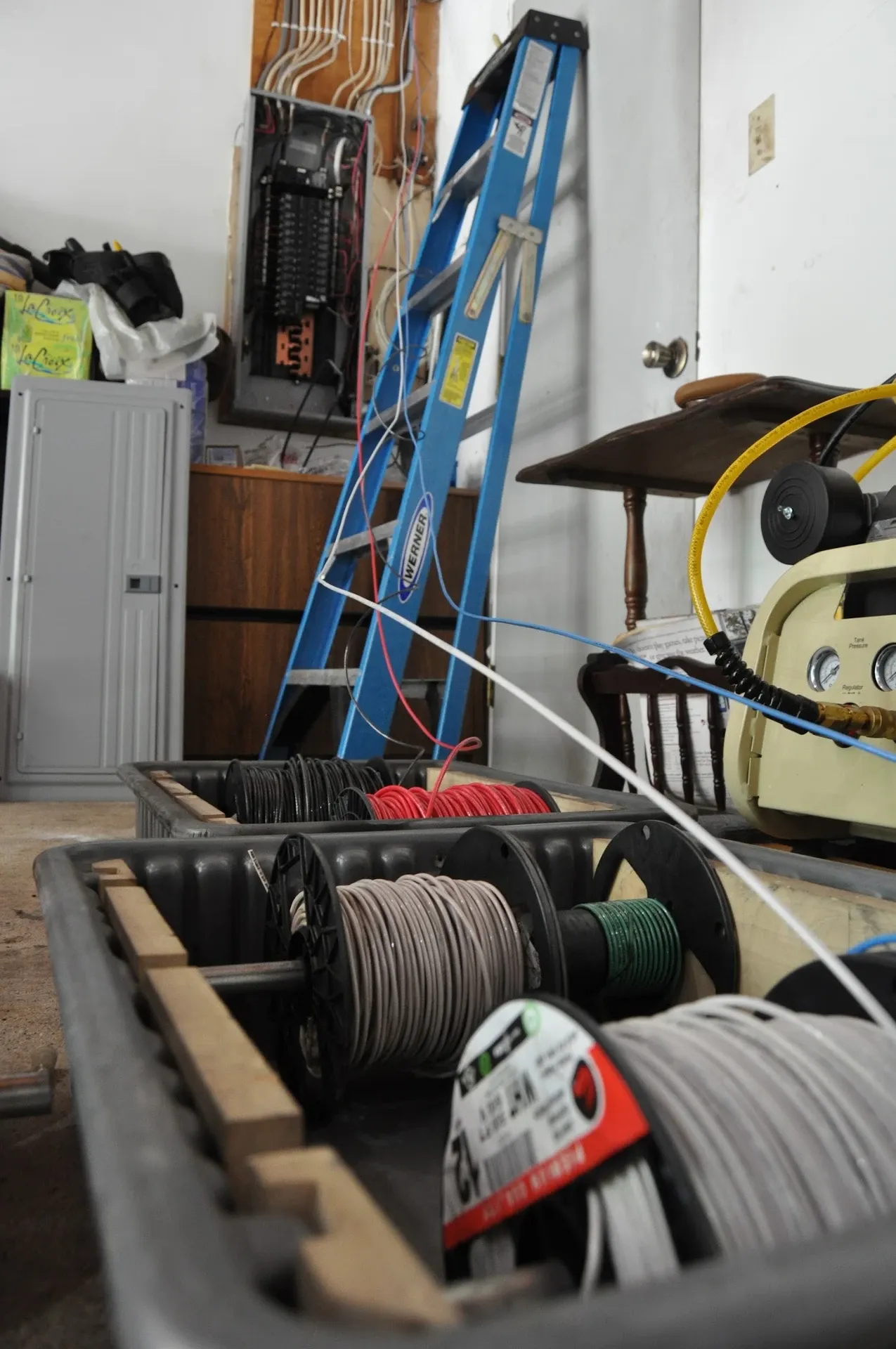 Electrical panel being wired in a utility room, with spools of new wire and a ladder nearby