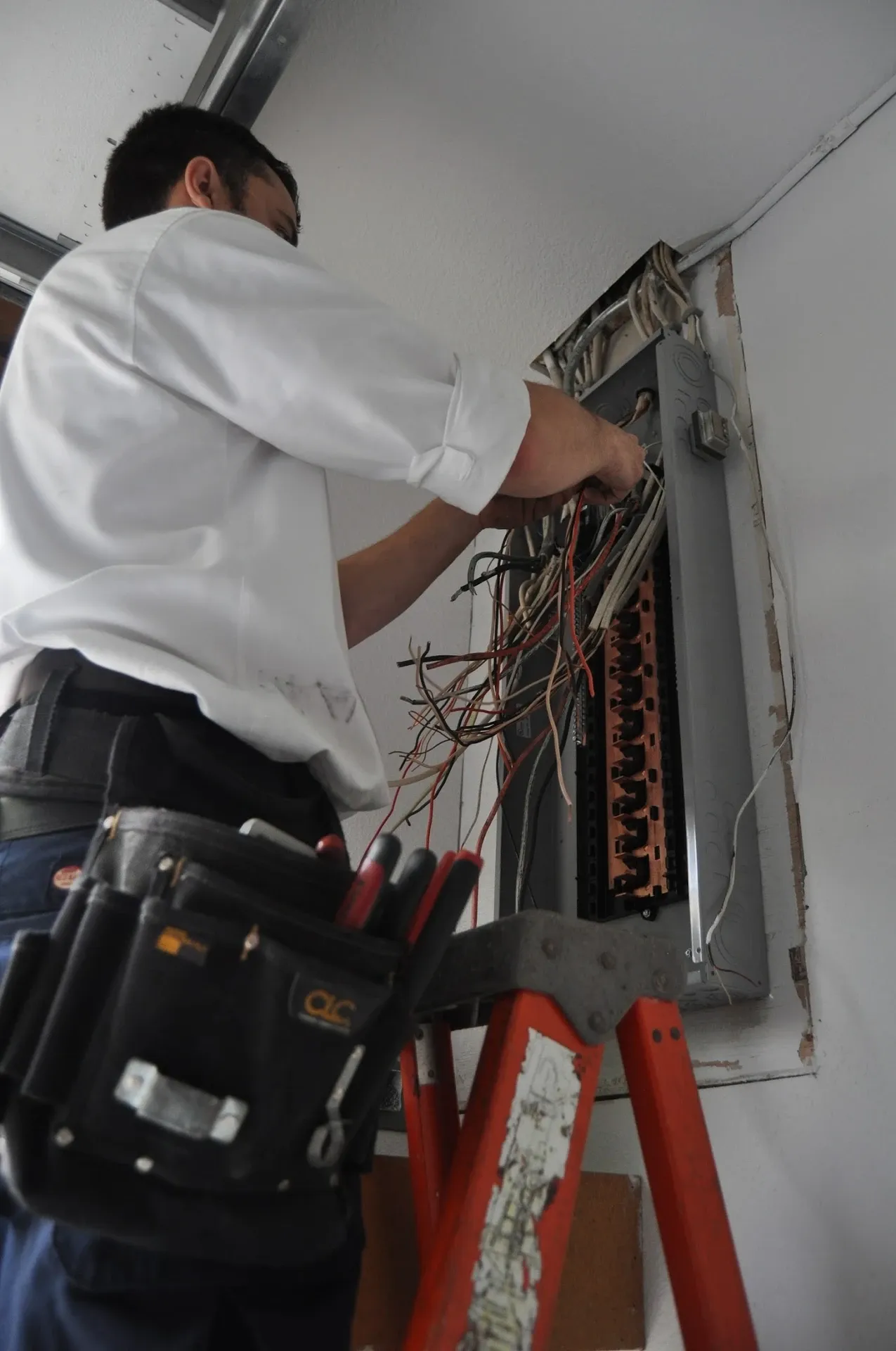 Harrison Electric technician on a ladder installing a new electrical panel