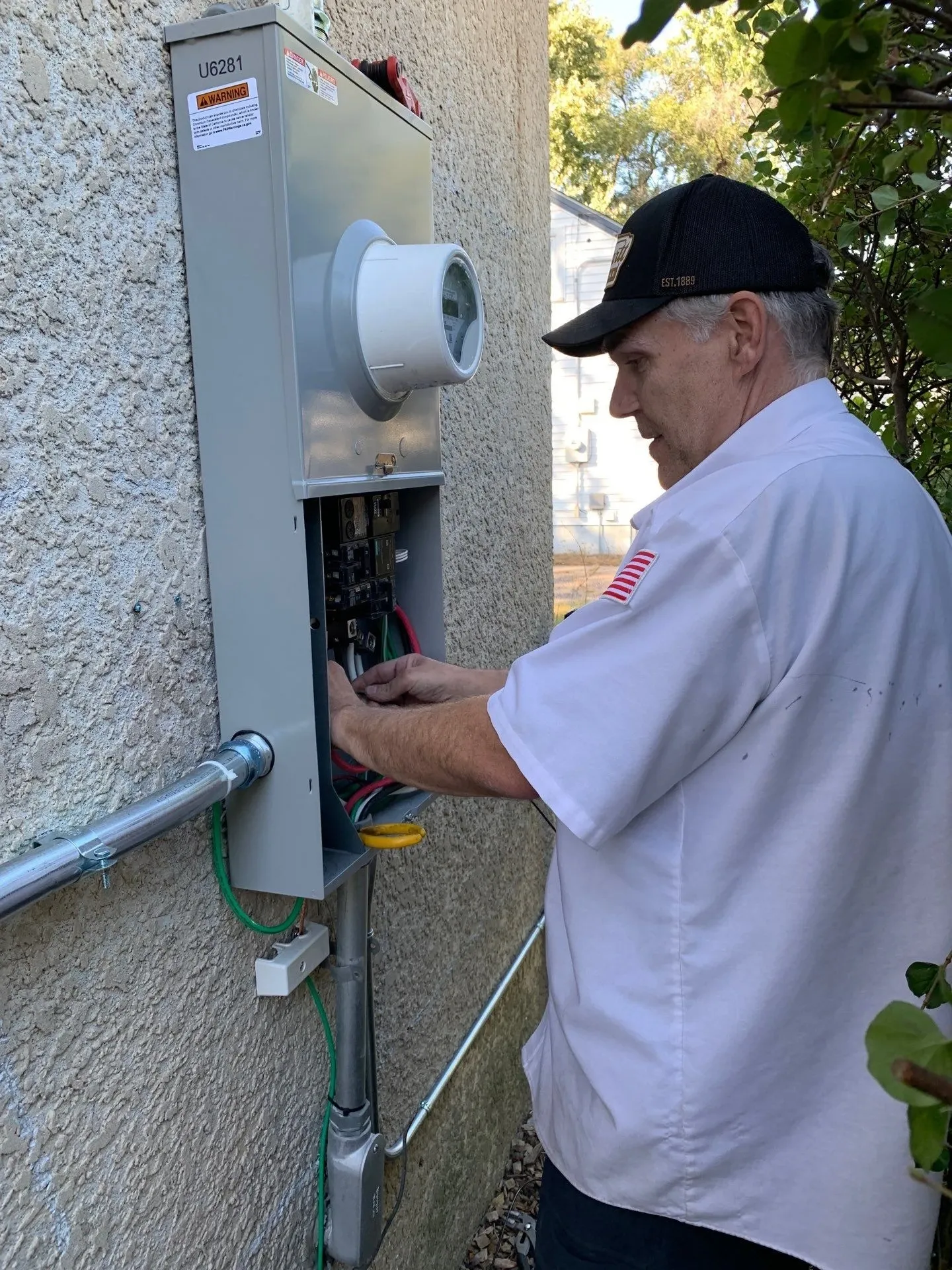 Harrison Electric electrician working at the electric meter and service equipment on a home's exterior wall