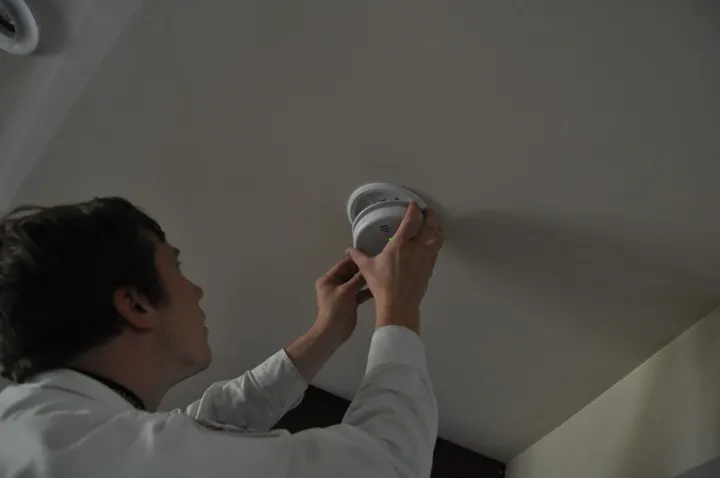 Harrison Electric technician installing a smoke alarm on a ceiling